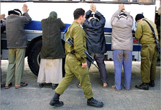 Blind-folded Palestinian men and women hold their arms up against a bus.